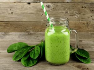Healthy green smoothie with spinach in a jar mug against a wood background